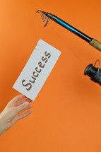 A fishing pole with a piece of paper with the word success on it 
