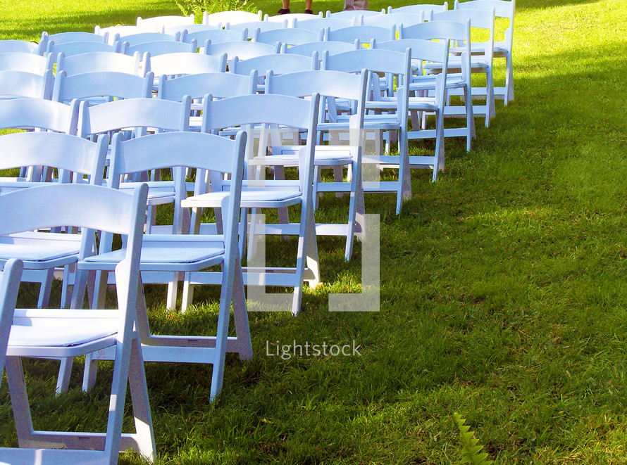 rows of white folding chairs in a lawn for a wedding, graduation commencement or outdoor gathering such as a wedding day in spring or summertime. 
