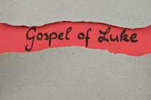 Gospel of Luke - torn open kraft paper over light red paper with the name of the Gospel of Luke