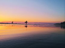 silhouettes of a surfers walking on a beach at sunset 