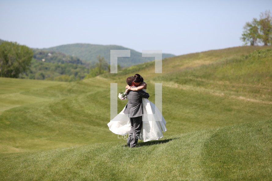 bride and groom hugging on green hills 