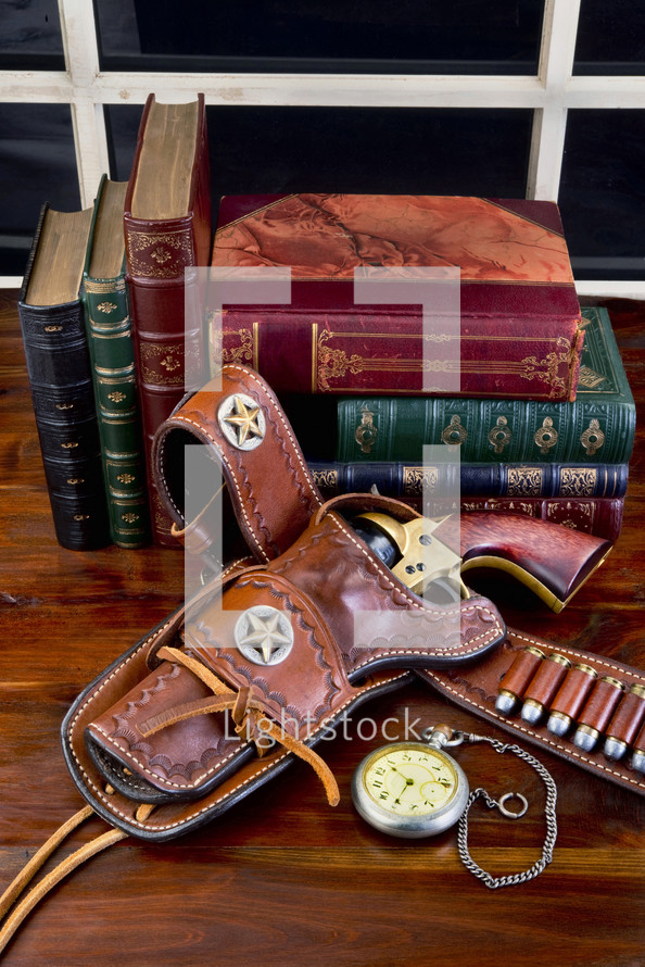 vintage guns in a holster and books on a wood table 