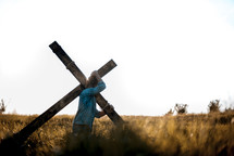 a man carrying a cross through a field 