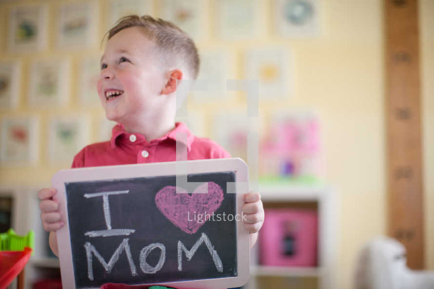 A little boy holding a chalkboard sign that reads I heart mom 