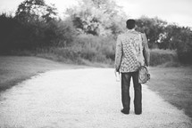man walking down a gravel road with a Bible 