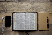 opened Bible, journal, coffee cup, pen, cellphone, and earbuds 