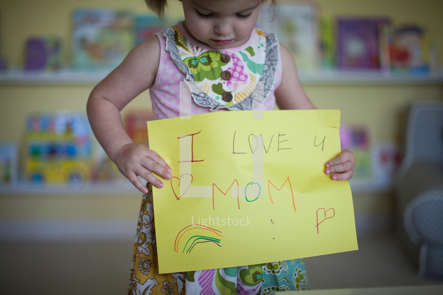 a little girl holding a sign that reads I love mom 