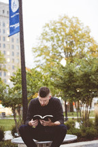 a man reading a Bible sitting outdoors 