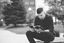 a man reading a Bible sitting outdoors 