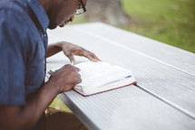 a man reading a Bible at a picnic table 