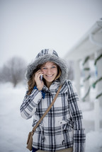a woman in a coat talking on a cellphone in the snow 