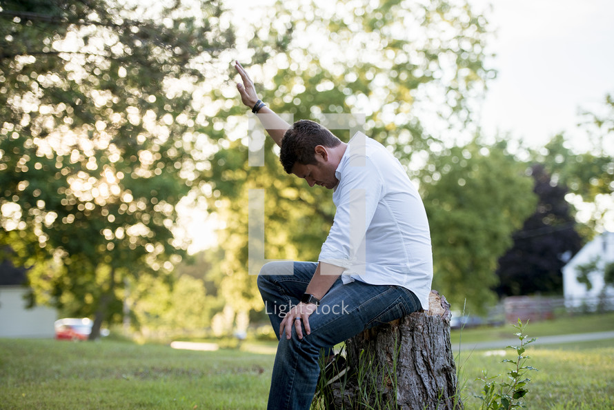 a man sitting on a tree stump with hand raised 