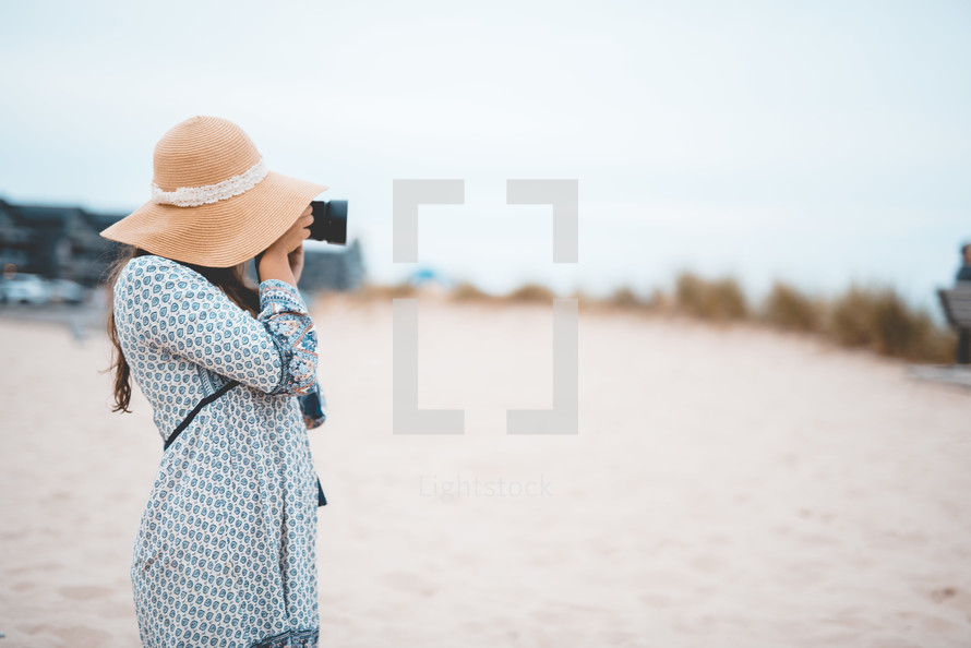 a woman standing on a beach taking pictures with a camera 