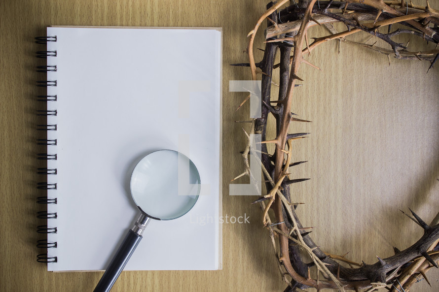 blank notepad, magnifying glass, and crown of thorns on a wood background 