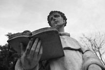 Outdoor statute of a priest reading a Bible.
