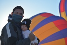 a father holding an infant and a hot air balloon 