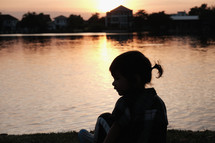 silhouette of a child by a pond at sunset 