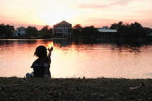 child sitting by a pond a sunset 