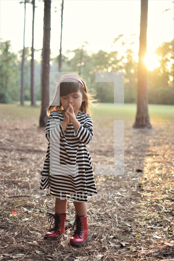 a toddler girl praying outdoors 