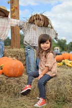 a little girl sitting on hay in a pumpkin patch 