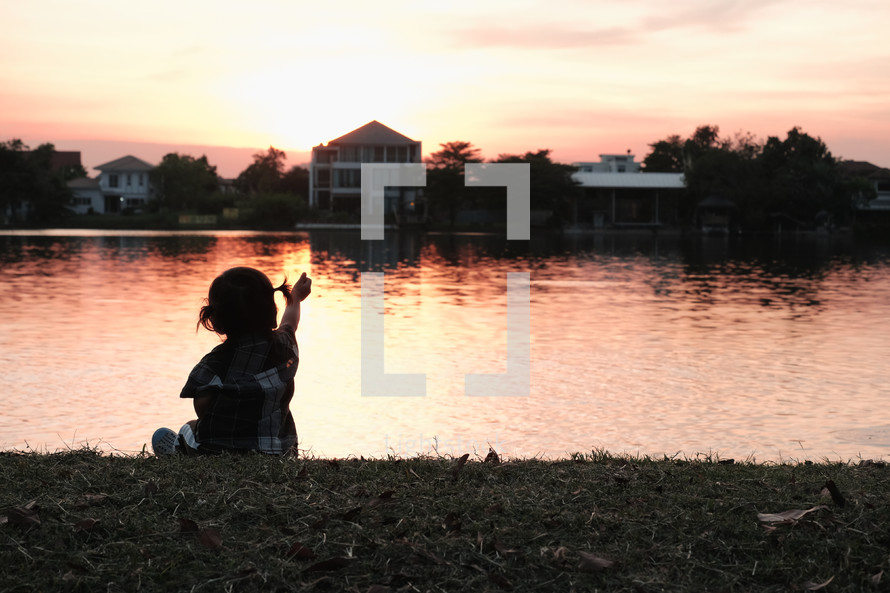 child sitting by a pond a sunset 