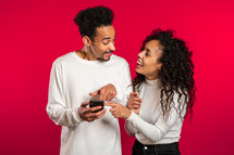 Young couple using mobile device. Man talking about apps and explains to girl how to use application. Red studio background.