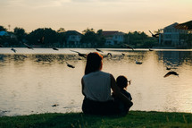 mother and daughter sitting by a pond at sunset 