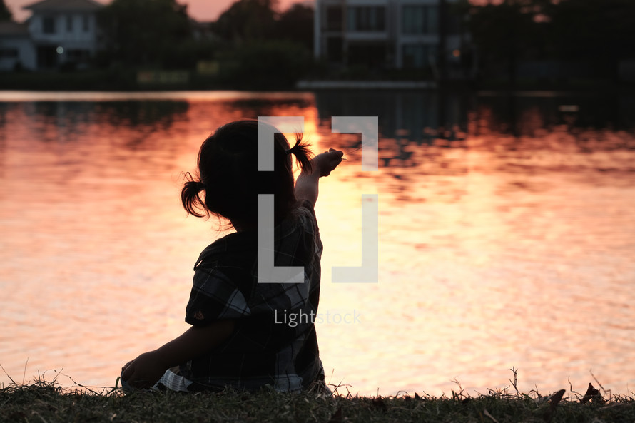 child sitting by a pond at sunset 