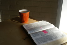 Open Bible on a table with a cup of coffee.