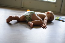 an infant in a diaper lying on a wood floor