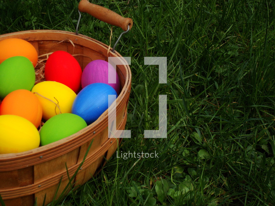 brightly colored Easter eggs in a basket in the grass 