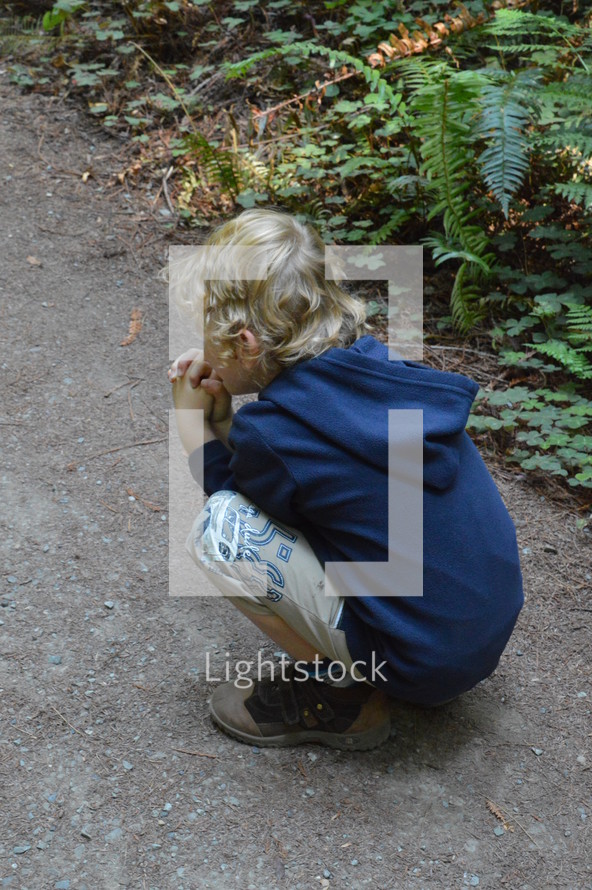 a boy squatting on a path praying 