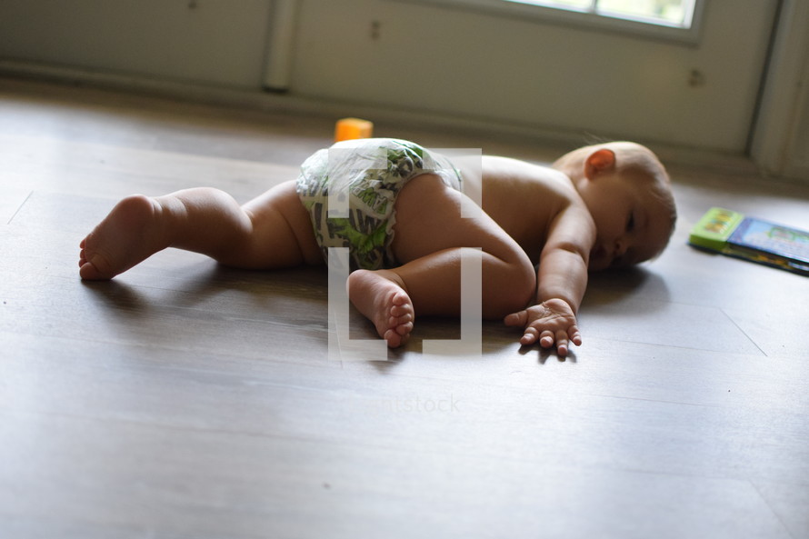 an infant in a diaper lying on a wood floor