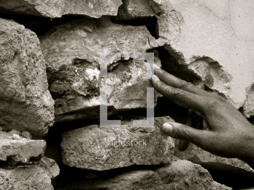 hand placing a stone in a wall