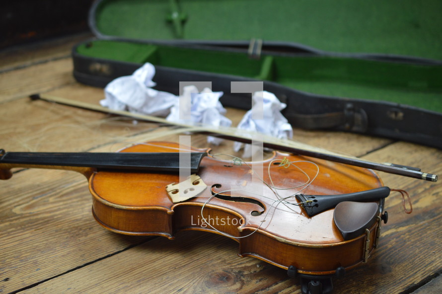 old broken violin on rural wooden floor with antique violin case and tattered fiddlestick