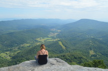 a woman sitting on a mountaintop thinking 