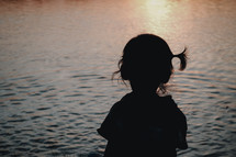 silhouette of a child sitting by a lake at sunset 