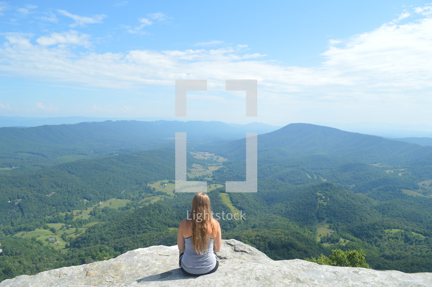 a woman sitting on a mountaintop thinking 