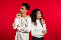 Portrait of young thinking pondering couple on red studio background. Man and woman look in different directions and everyone thinks about his problem