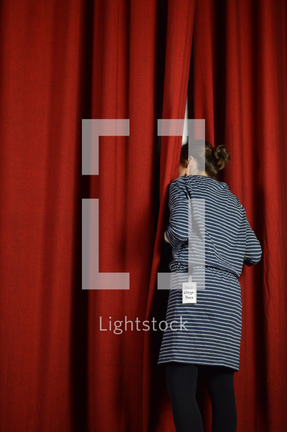 woman with a back stage pass looking behind the red curtains on a stage