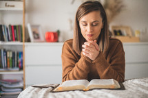 woman praying bedside in front of an open Bible 