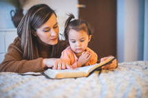 a mother reading the Bible to her toddler daughter 