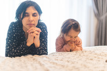 mother and toddler daughter praying bedside 
