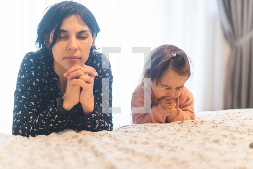 mother and toddler daughter praying bedside 