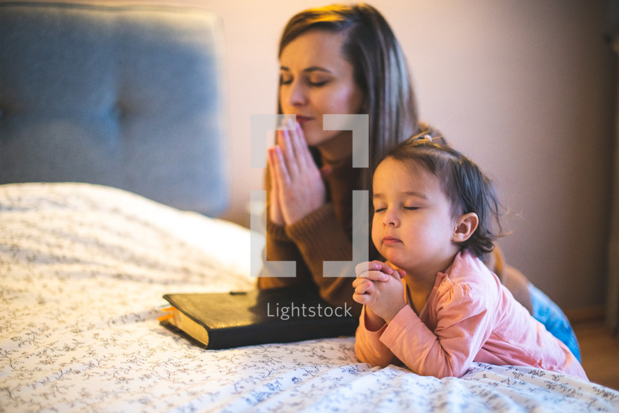 mother and daughter praying bedside 