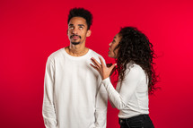 african woman emotionally screaming at her husband or boyfriend on red background in studio. Bored man rolling his eyes. Concept of conflict, problems in relationships