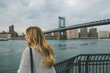 A woman stands at a railing looking out over a bay near a bridge.
