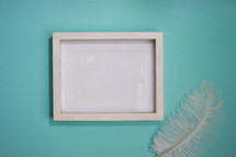 Blank white frame on turquoise background with feather