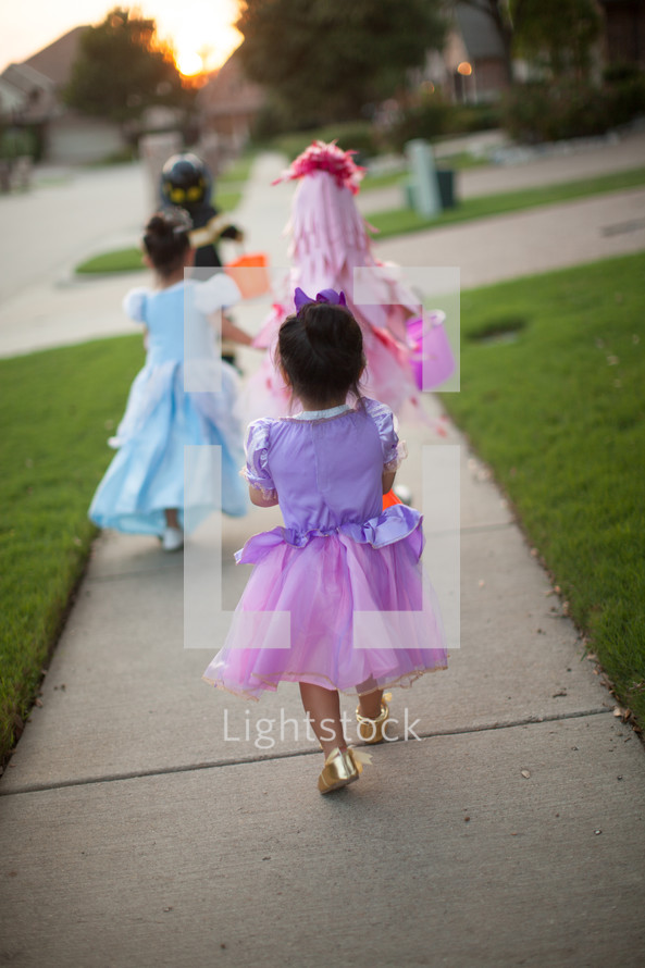 children trick or treating on a neighborhood sidewalk on Halloween 