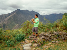 man playing a pipe on a mountain in South America 